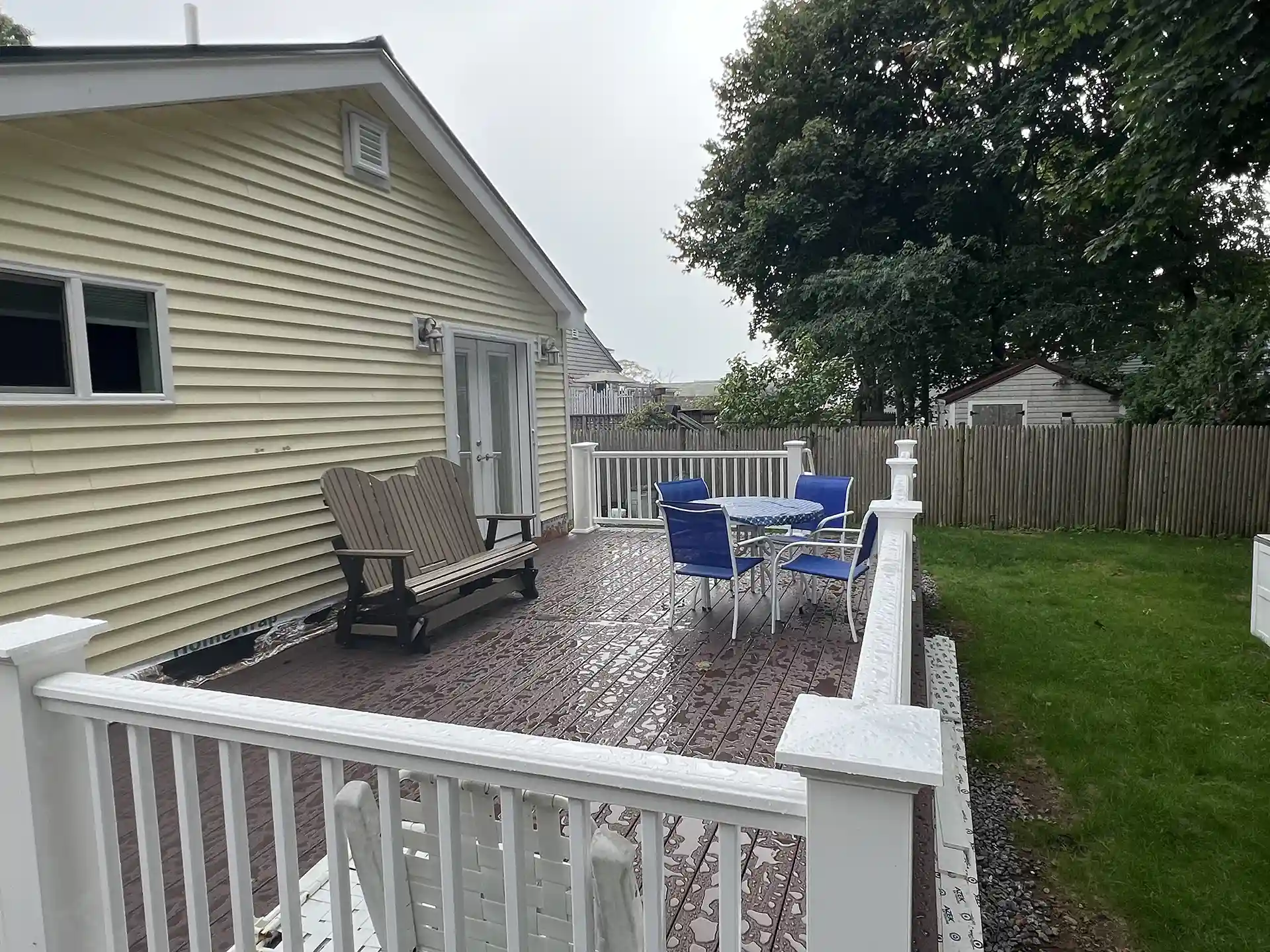 Photo of a spacious deck with white railing, a table set with blue chairs, and a wooden bench.
