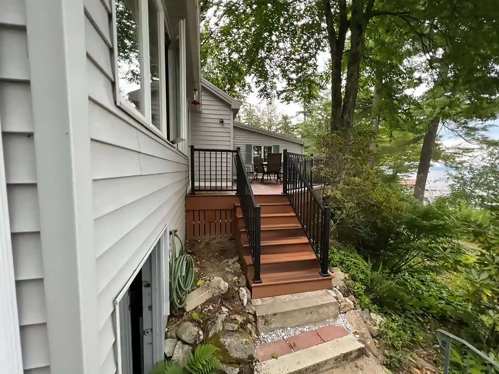 Photo of a deck with stairs leading to a lower level, black railing, and a natural landscape.
