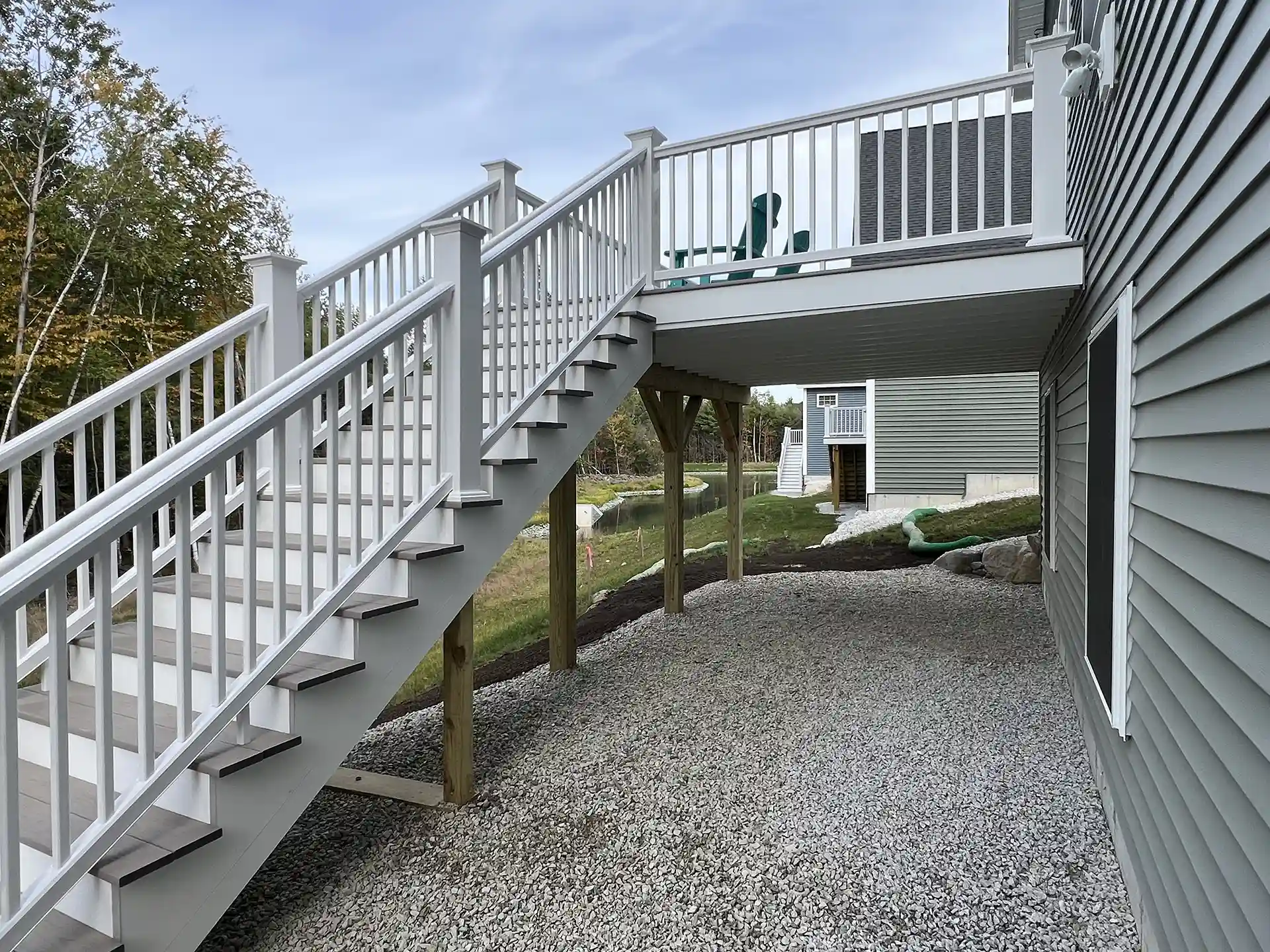 Photo of a raised deck with white railing and stairs leading to a gravel area below.

