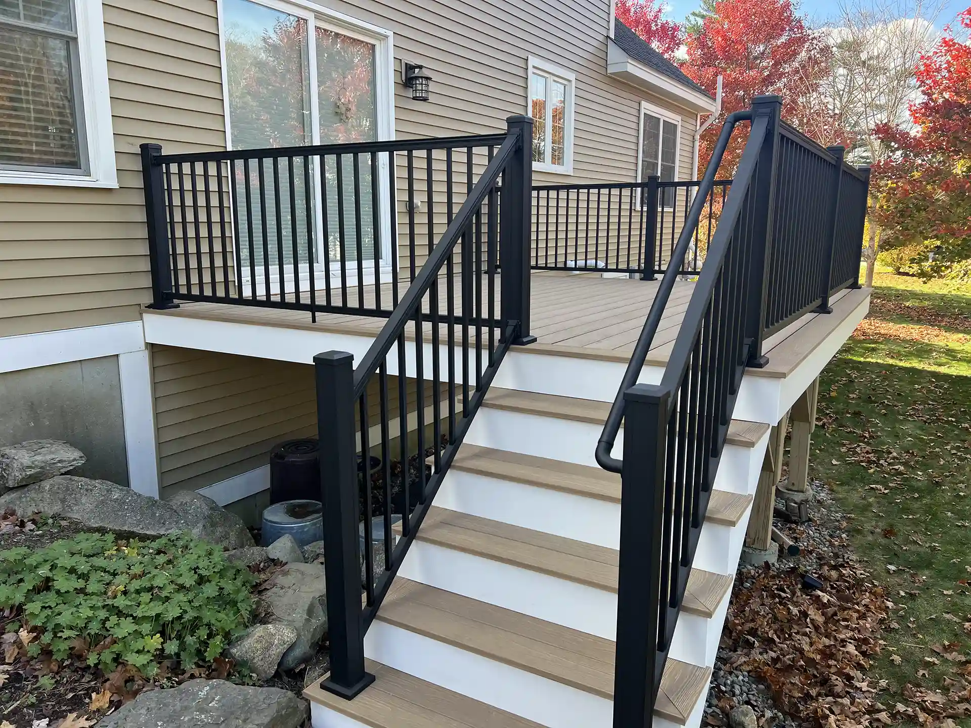 Photo of a deck with a tan surface, black railing, and stairs leading down to the yard.
