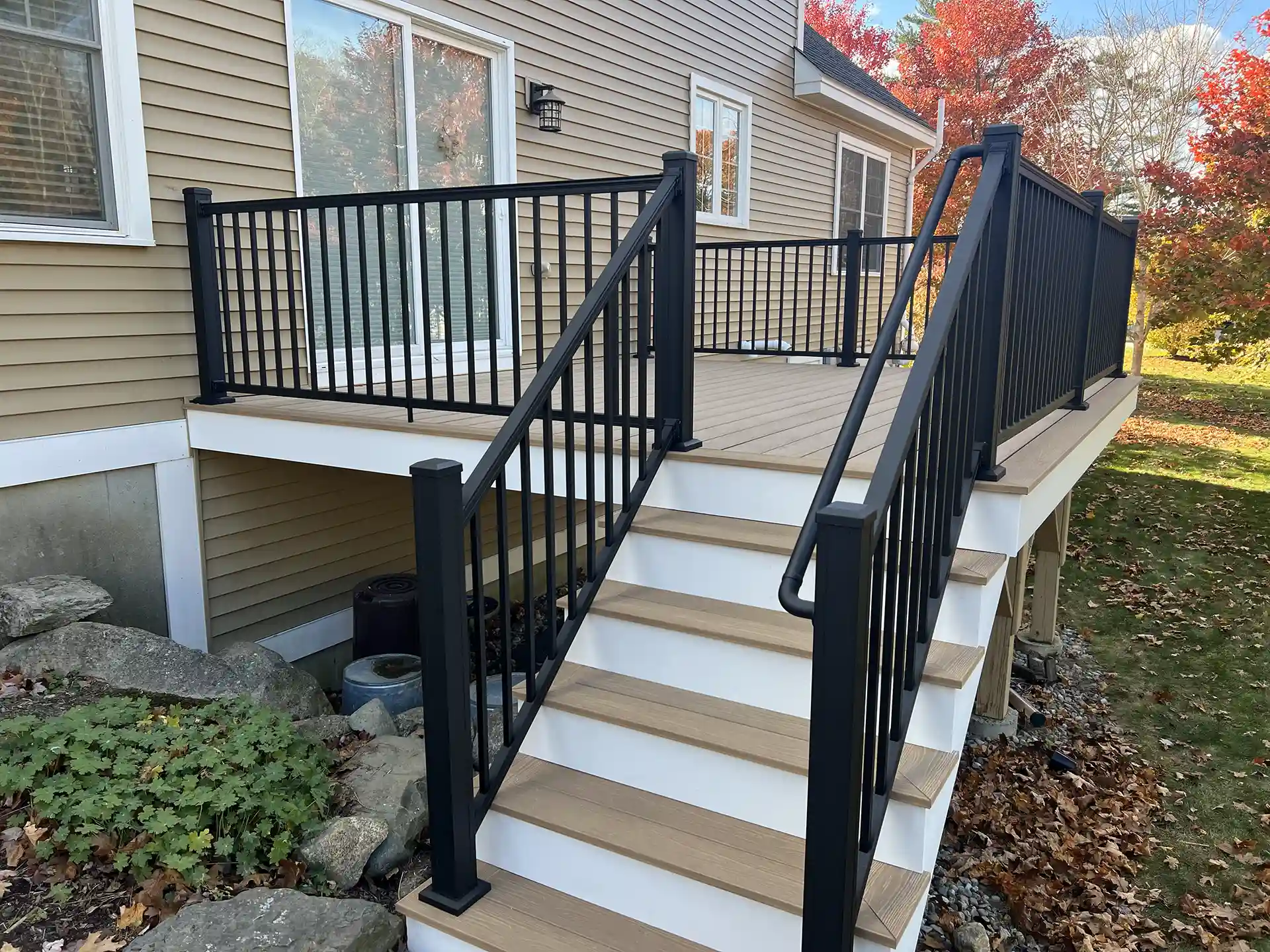 Photo of a raised composite deck with black railings and stairs leading to a fall backyard.
