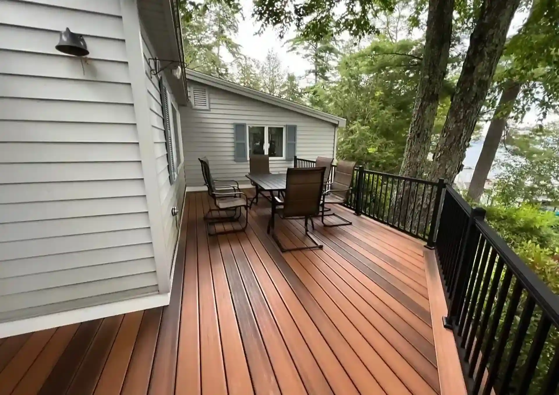 Photo of a narrow composite deck with dining furniture and black railings overlooking a wooded lake view.
