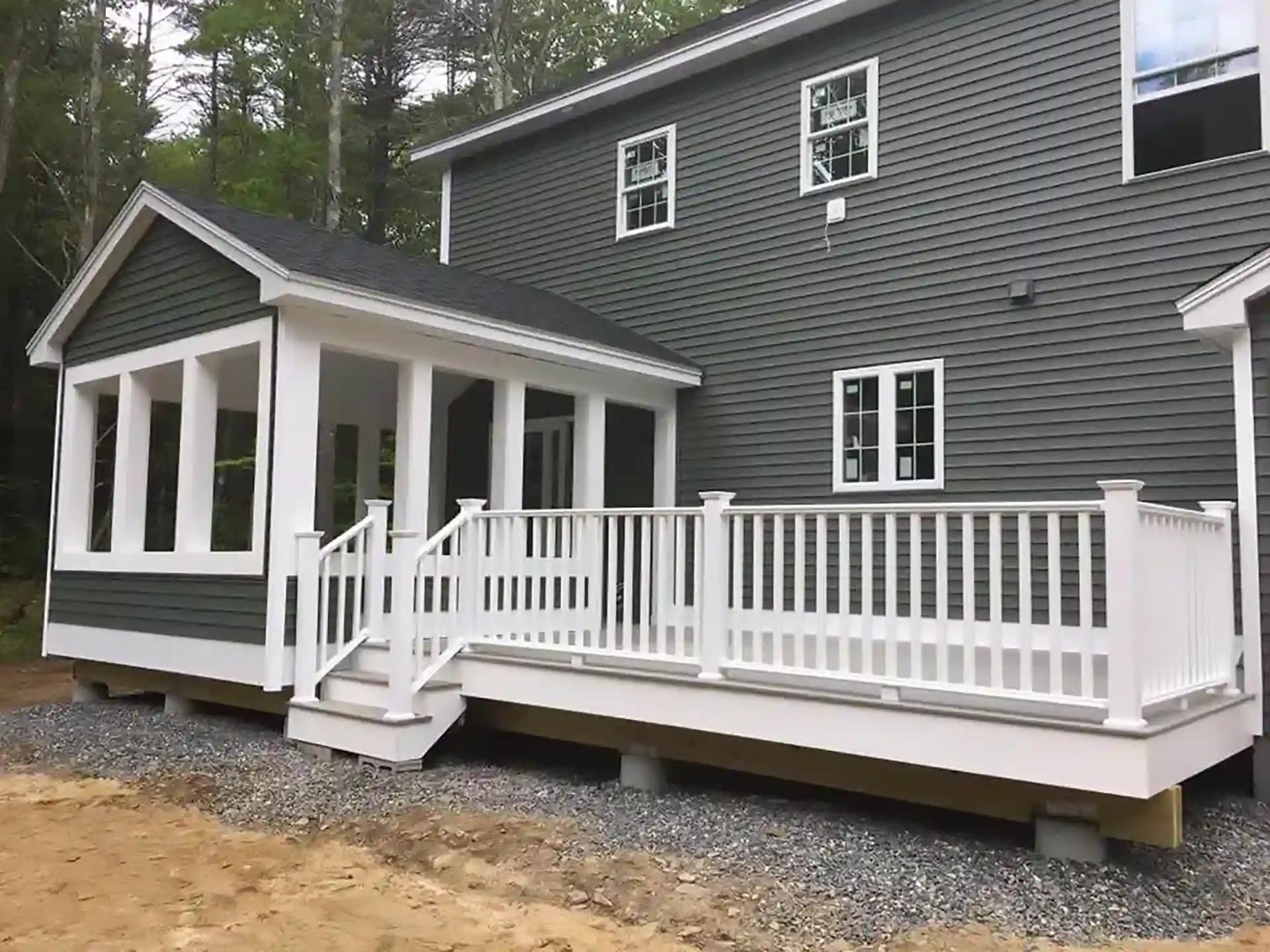 Photo of a screened porch and adjacent open deck with white railings on a green-sided home.
