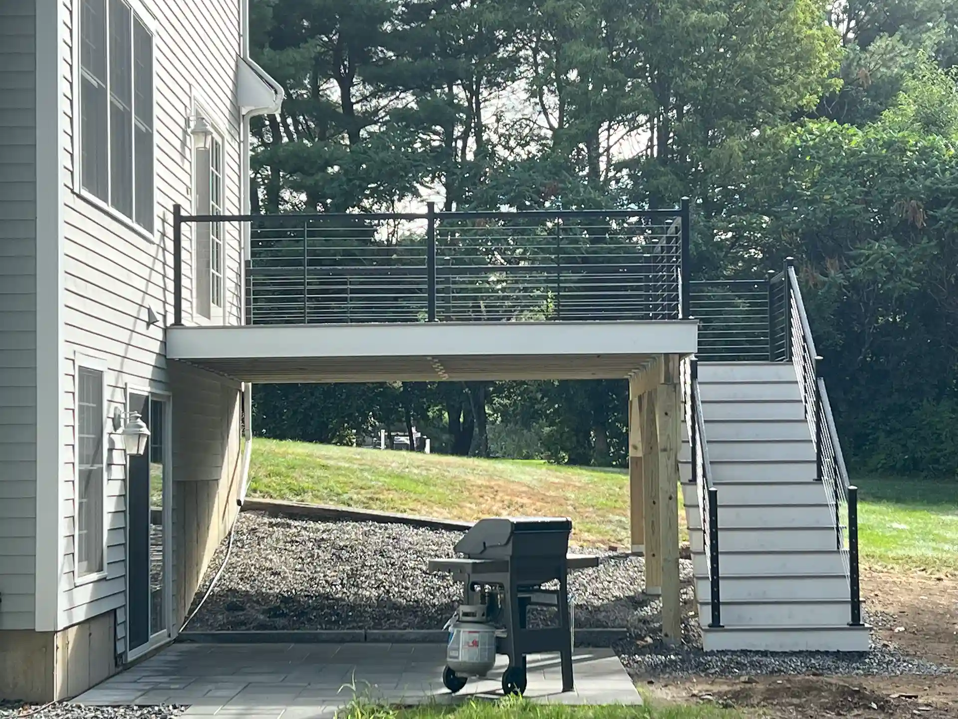 Photo of a raised deck with cable railings, wide stairs, and an under-deck grilling area.
