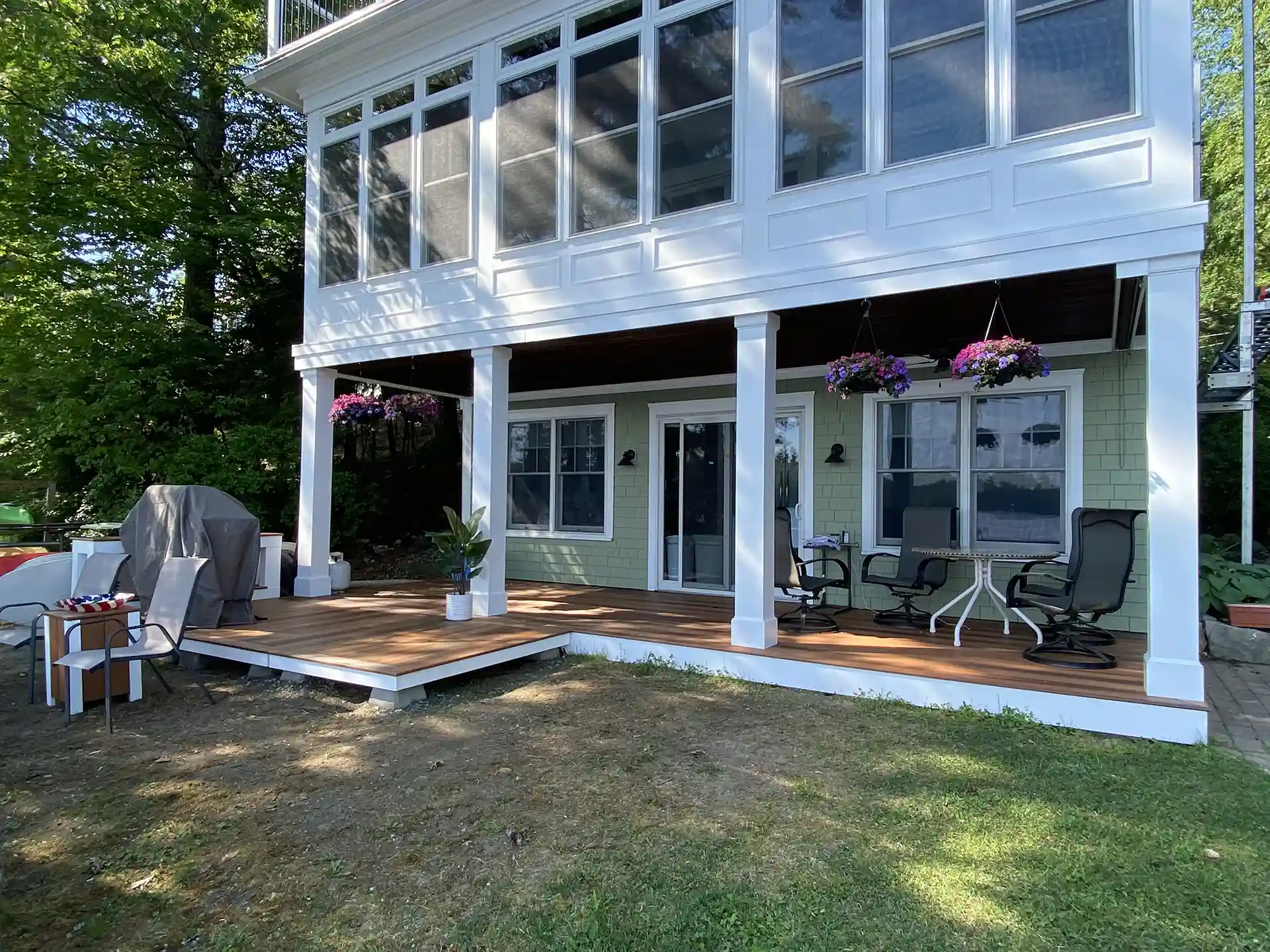 Photo of a ground-level covered deck with composite flooring, lounge seating, grill, and hanging planters.
