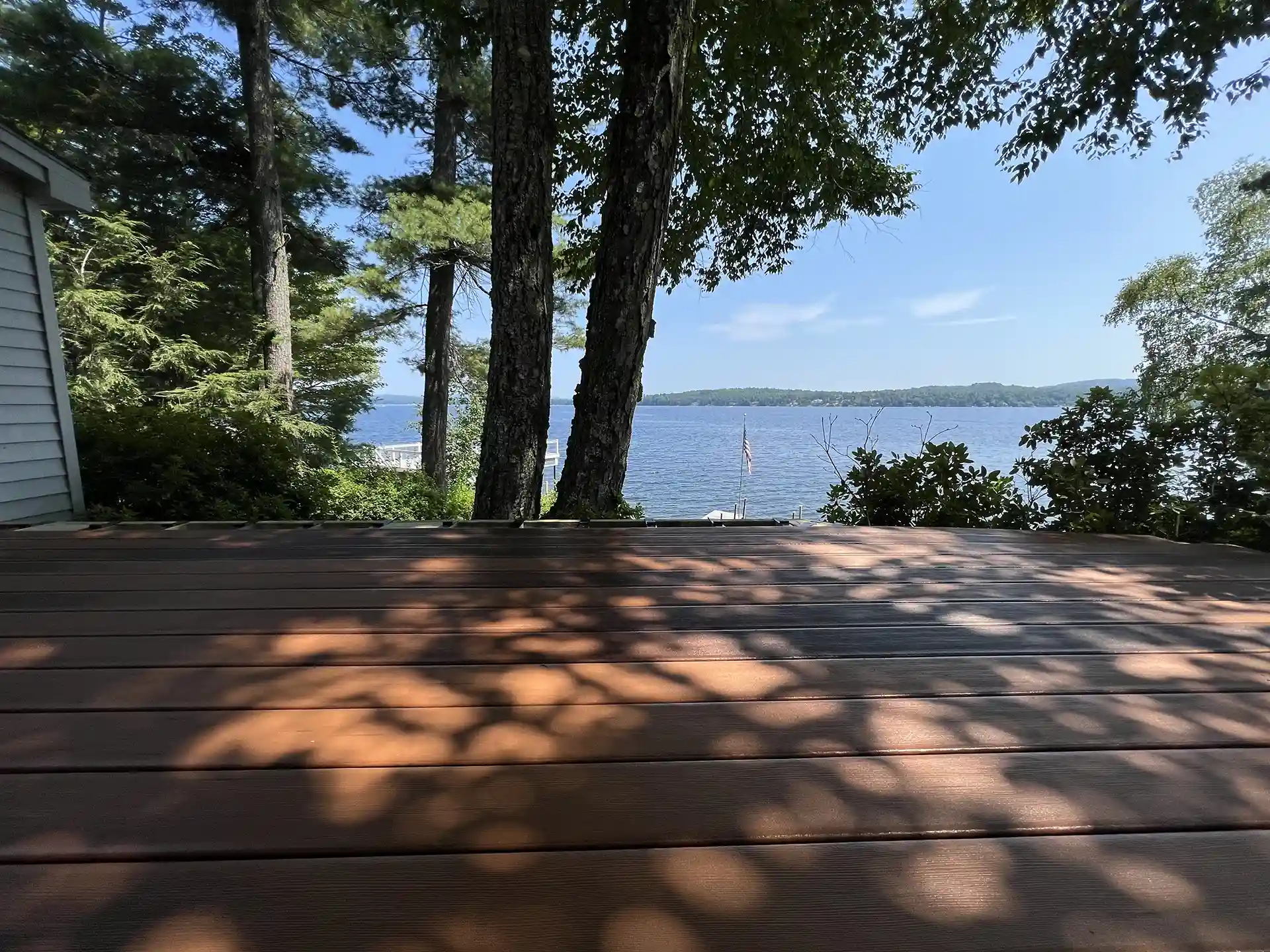 Photo of a low-profile composite deck with shade trees and a lake view in the background.

