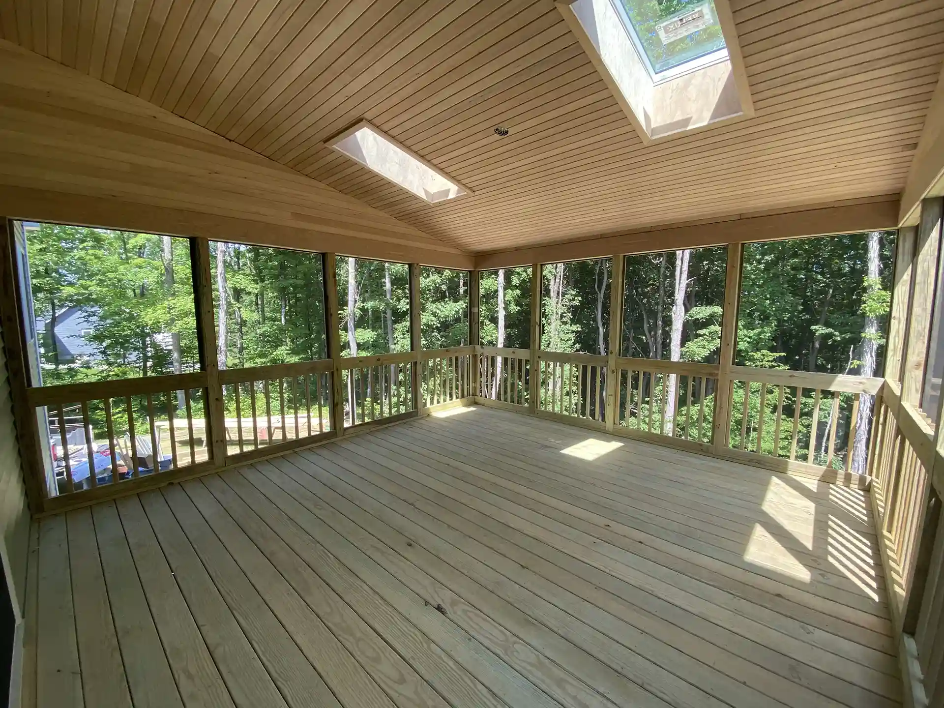 Photo of a screened-in wood porch with skylights and views of surrounding trees.
